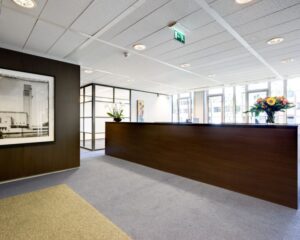 Moderne kantoorreceptie met houten balie, grote ramen en bloemen op het bureau.