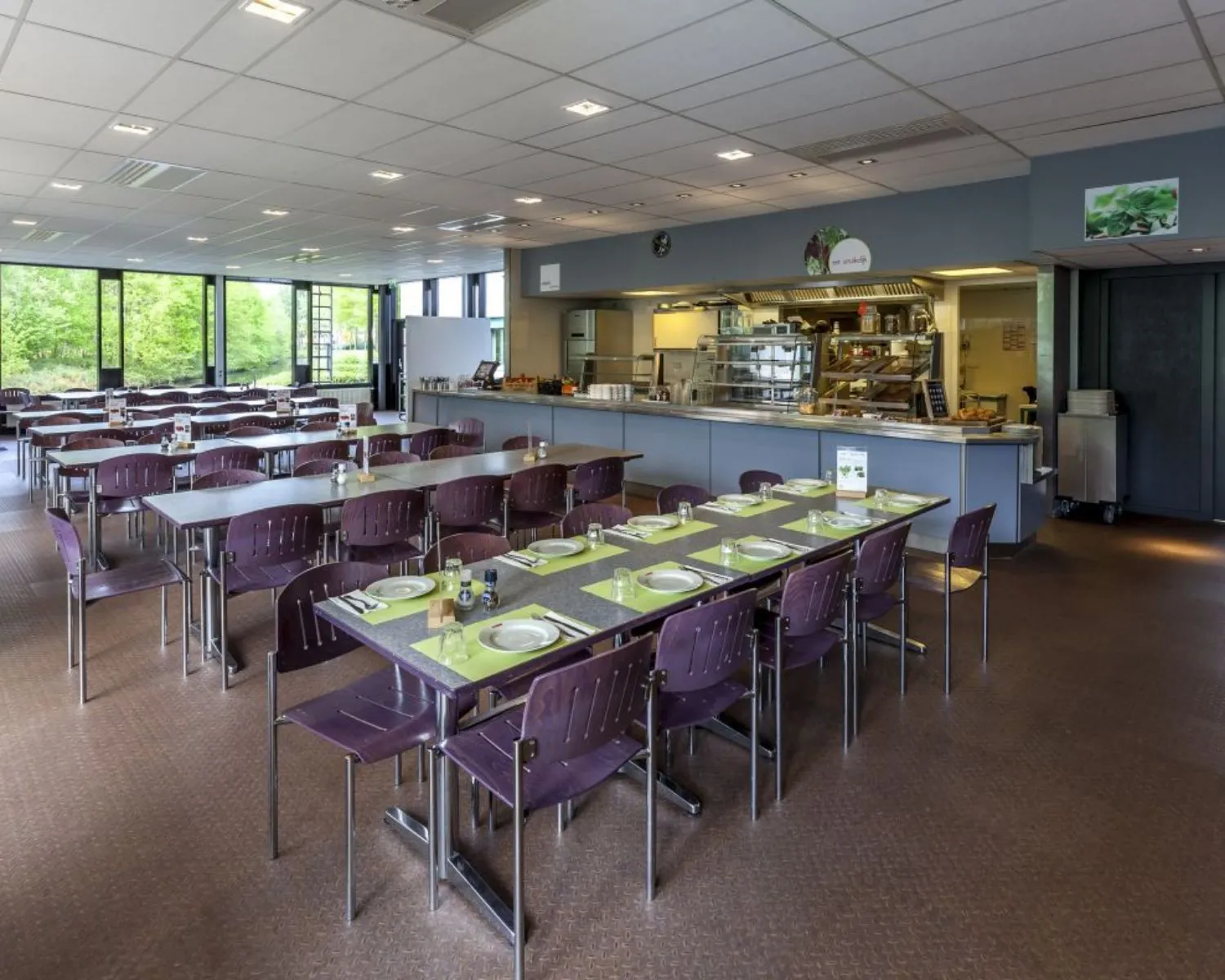Moderne bedrijfs- of schoolkantine met gedekte tafels en een zelfbedieningsbuffet.
