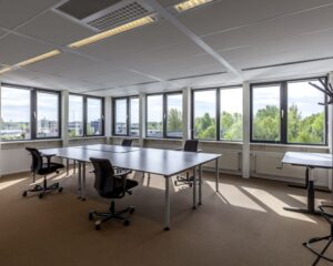 Lichte, moderne kantoorruimte met grote ramen, meerdere bureaus en bureaustoelen.