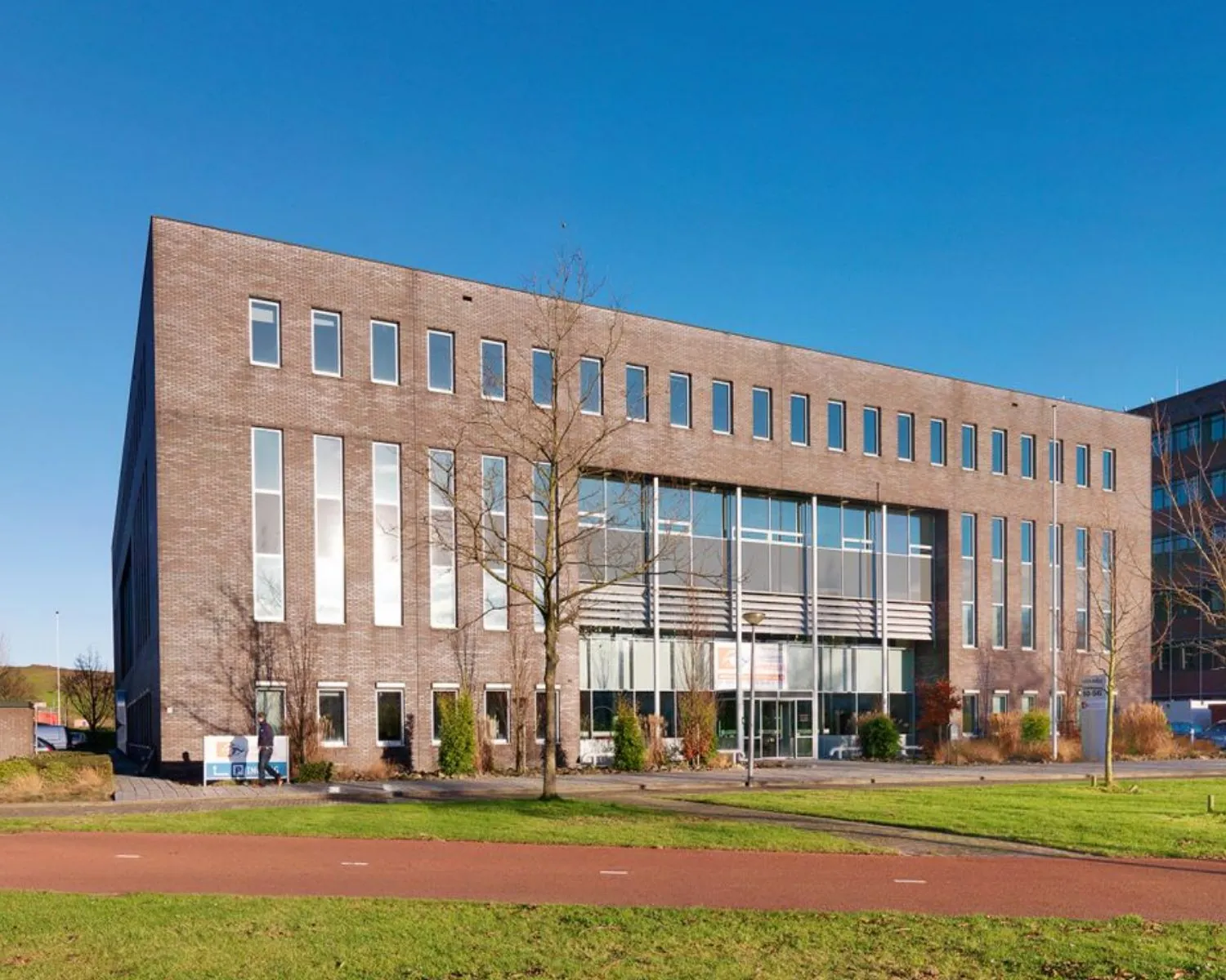 Modern kantoorgebouw met grote ramen en een bakstenen gevel, gefotografeerd op een zonnige dag.