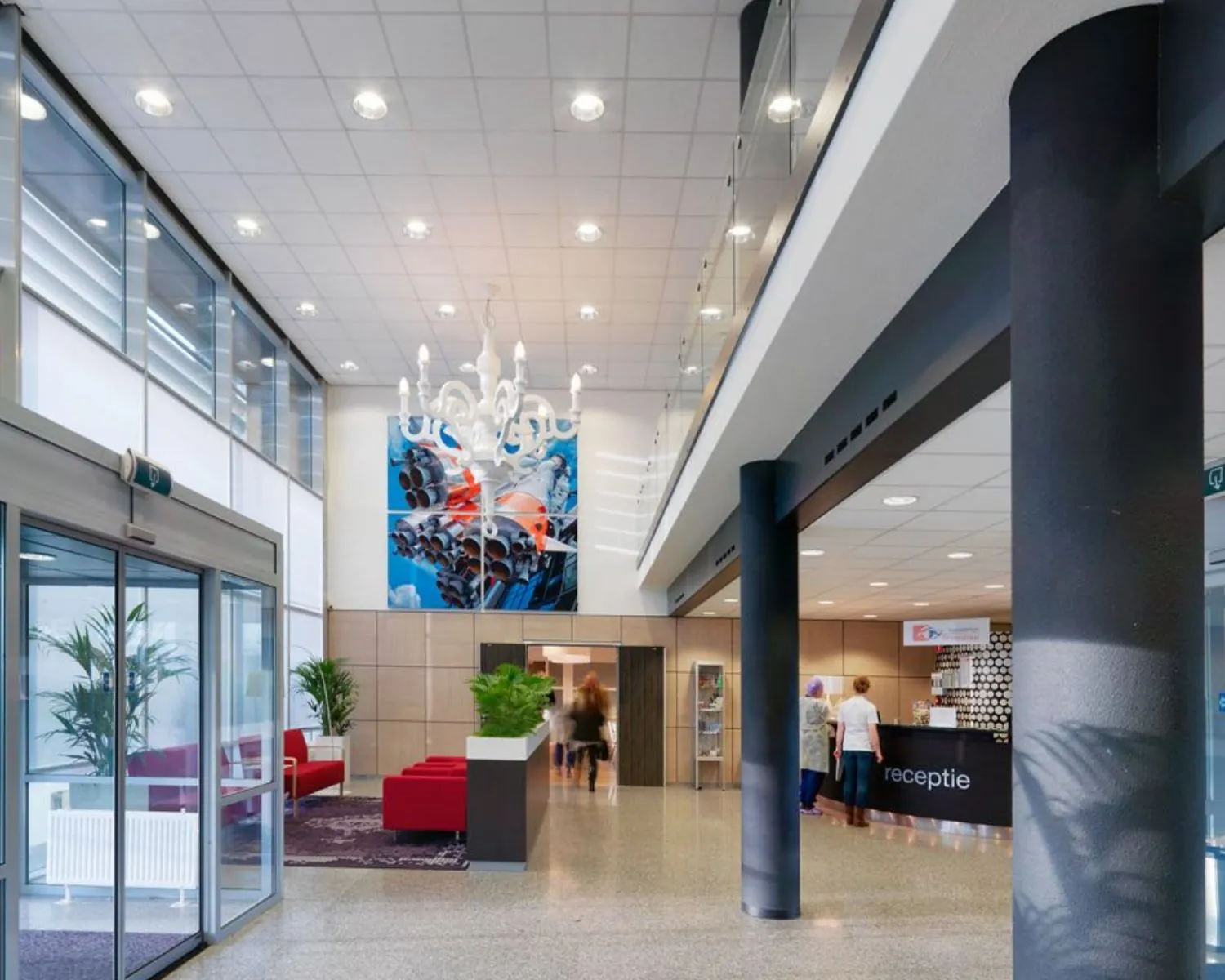 Moderne en lichte ontvangsthal met receptiebalie, zitgedeelte en kleurrijk kunstwerk aan de muur.