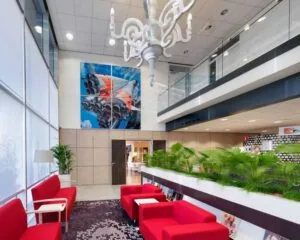 Moderne wachtruimte met rode zitmeubels, grote muurfoto van een raketmotor en veel groen.