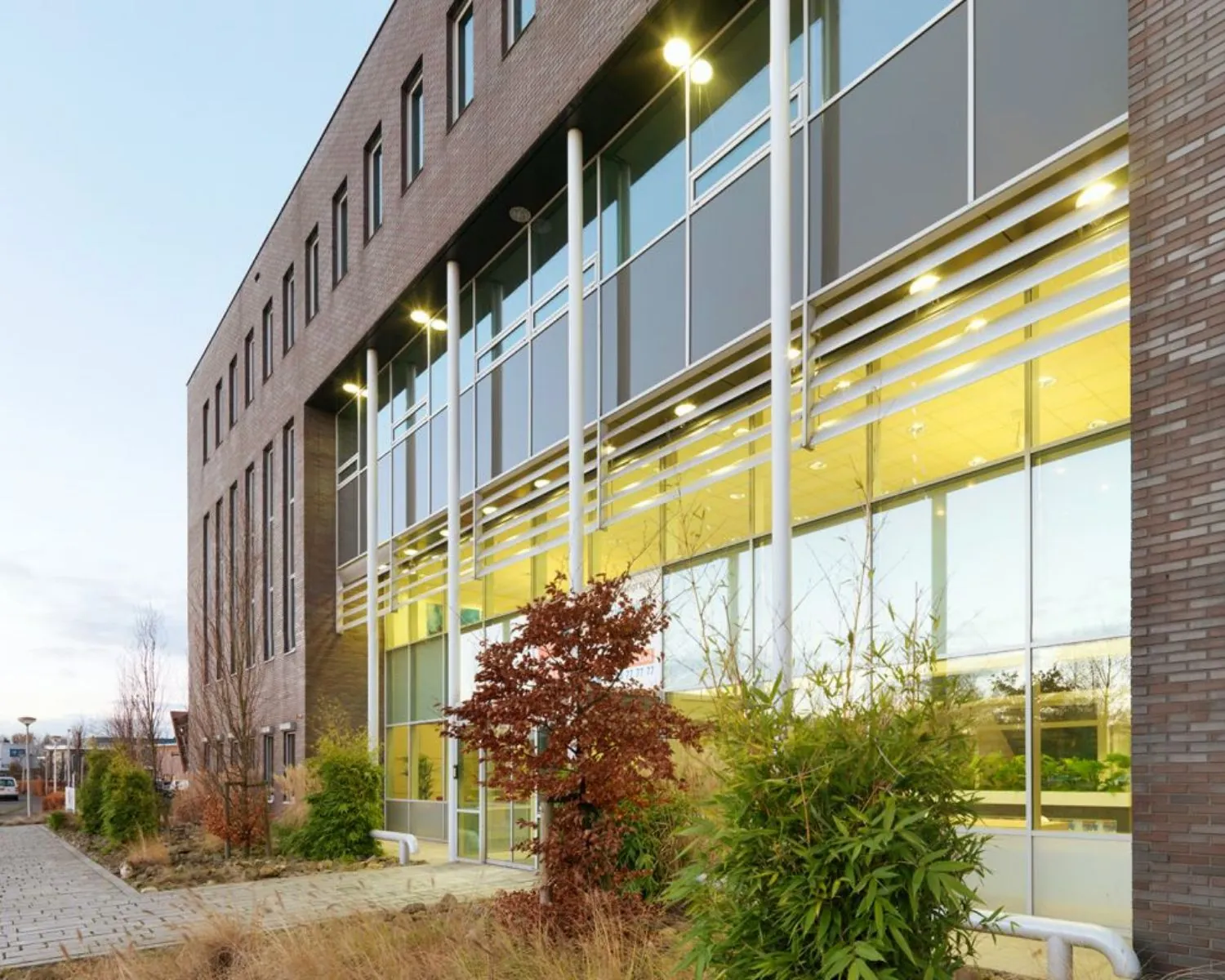 Moderne kantoorgebouw met grote ramen en planten langs de gevel.