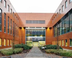 Moderne kantoor- of onderwijsgebouw met houten gevelbekleding en glazen entree, gefotografeerd vanaf een binnentuin.