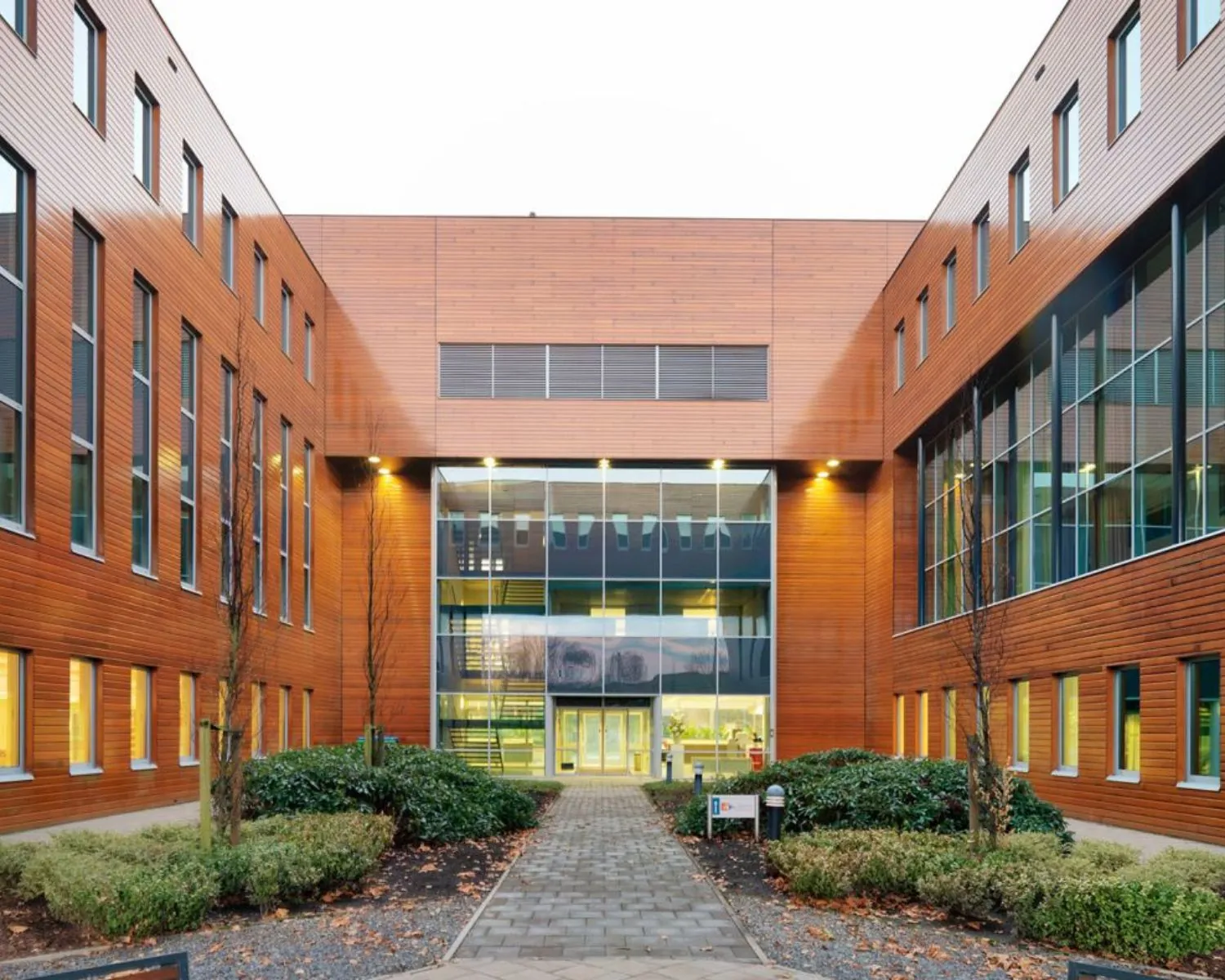 Moderne kantoor- of onderwijsgebouw met houten gevelbekleding en glazen entree, gefotografeerd vanaf een binnentuin.