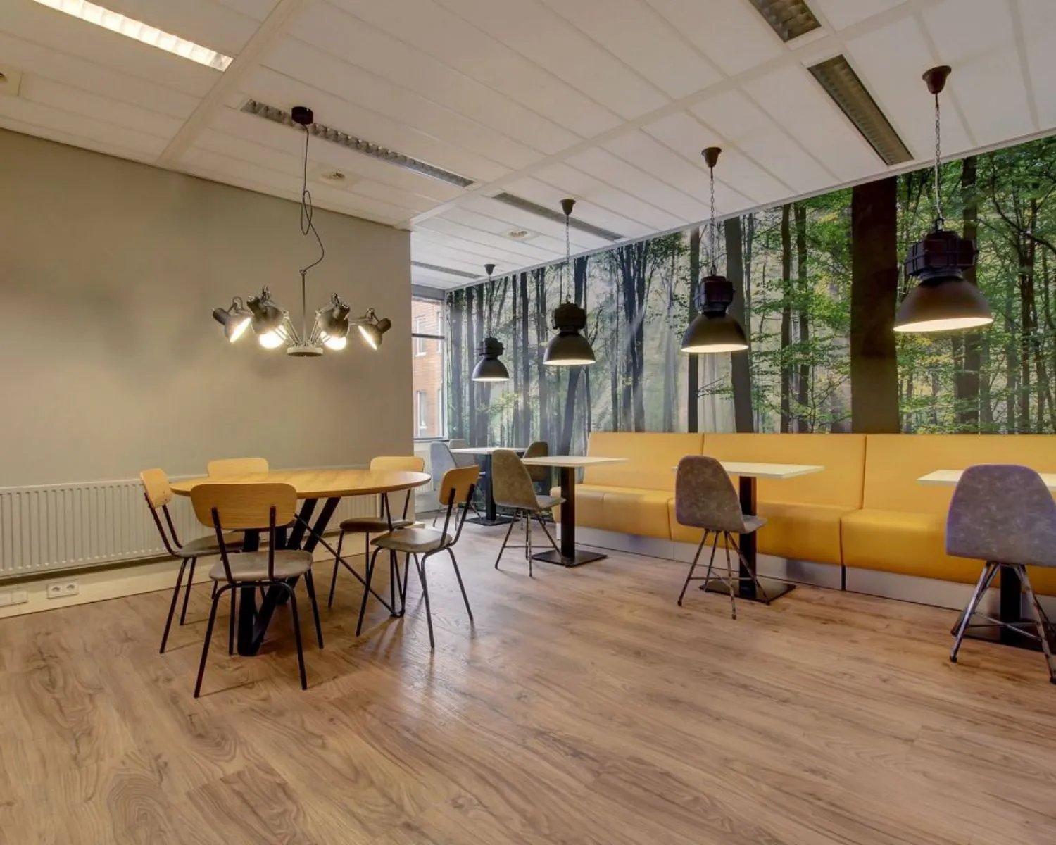 Moderne kantineruimte met houten vloer, gele banken en een wanddecoratie van een boslandschap.