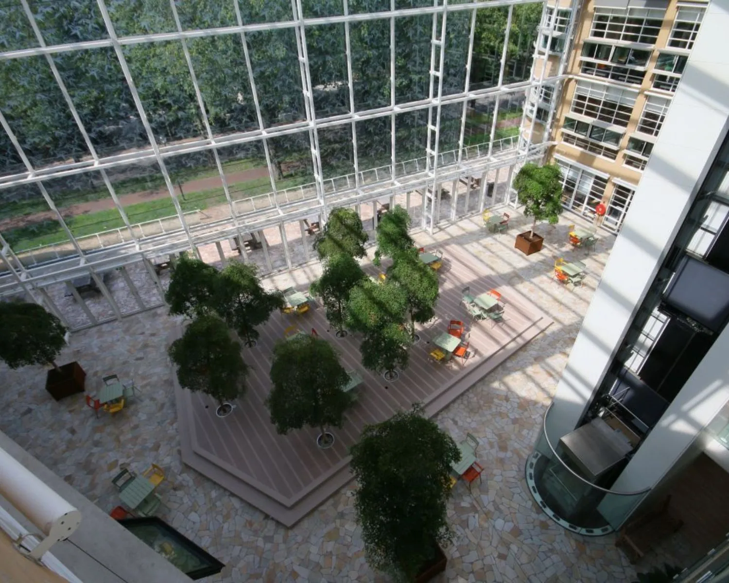 Zonnige binnentuin met veel groen, zitplekken en glazen gevel in een modern kantoorgebouw.