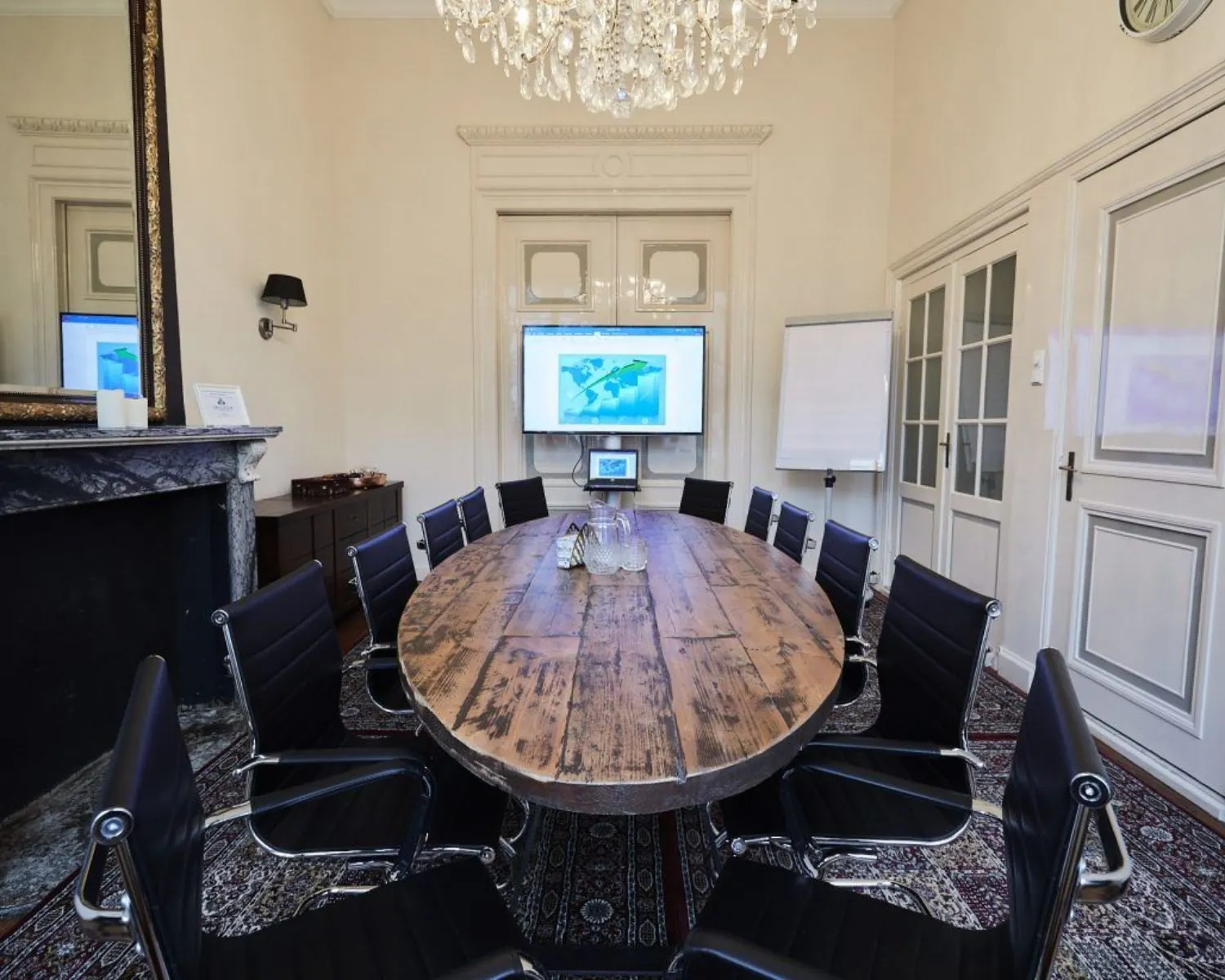 Vergaderruimte met een ovale houten tafel, moderne zwarte stoelen, een groot presentatiescherm en klassieke inrichting.