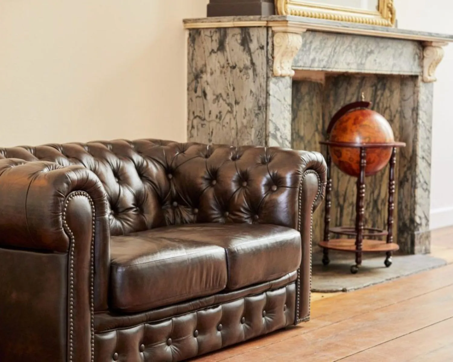 Donkerbruine leren Chesterfield-bank voor een marmeren open haard met een klassieke globe op standaard.