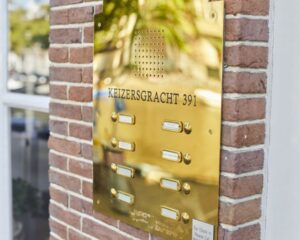 Gouden intercom- en belpaneel met het adres Keizersgracht 391 op een bakstenen gevel.