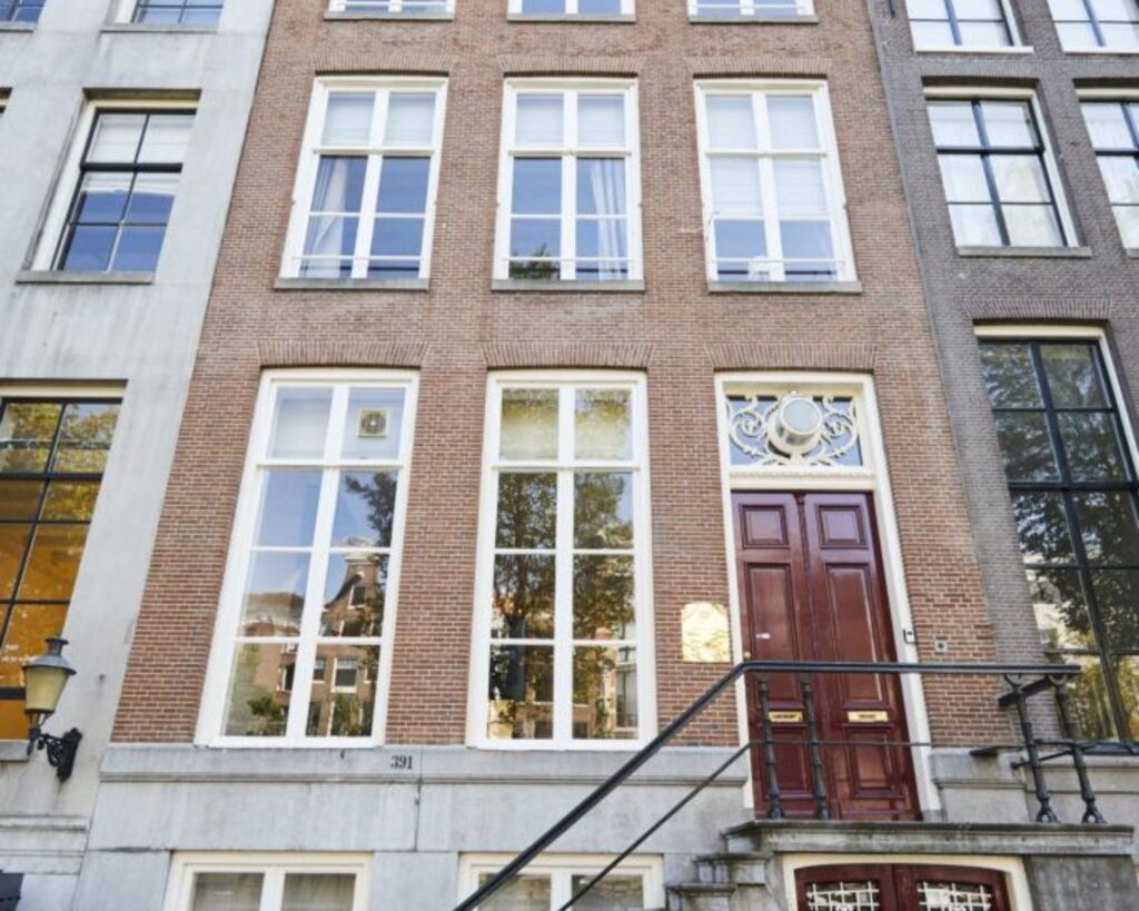 Gevel van een klassiek Amsterdams grachtenpand met hoge ramen en een dubbele houten voordeur.