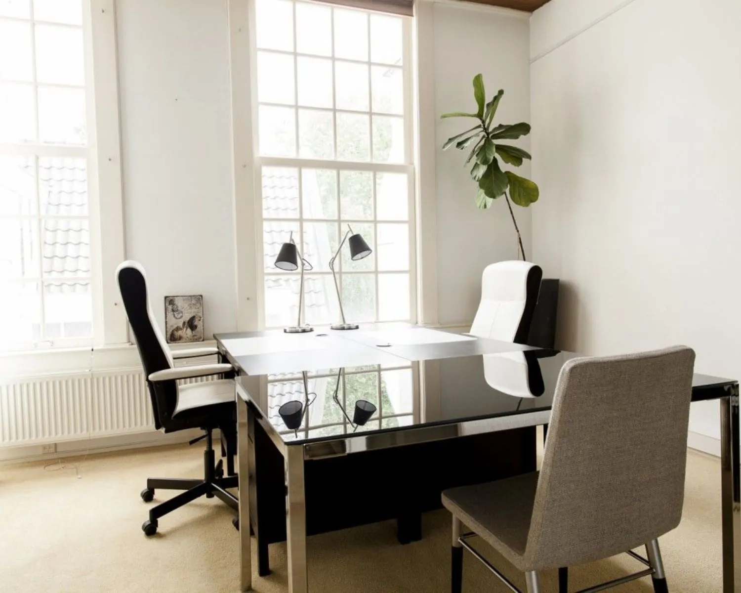 Modern en licht kantoor met grote ramen, een glazen bureau, drie stoelen en een kamerplant.