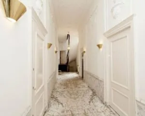 Luxe marmeren hal met witte wanden, gouden wandlampen en een houten trap aan het einde.