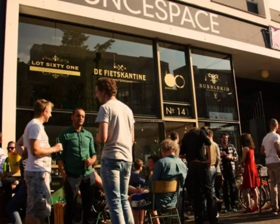 Groep mensen geniet van een zonnige middag voor De Fietskantine bij Number 141 in Amsterdam.