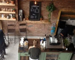 Barista bereidt koffie achter een vintage toonbank in een hippe koffiebar met bakstenen muur en het menu van Lot Sixty One.