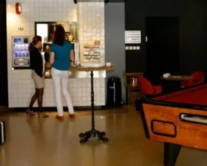 Twee vrouwen staan bij een koffie- en theeautomaat in een moderne, ontspanningsruimte met een pooltafel.