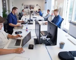 Een groep mannen werkt achter computers in een modern, licht kantoor met grote ramen en minimalistische inrichting.