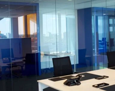 Modern kantoorinterieur met glazen wanden, bureaus, bureaustoelen en telefonieapparatuur.