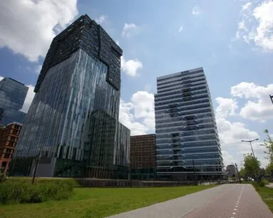 Twee moderne kantoorgebouwen, waaronder het RBS-gebouw, aan een fietspad met gras en blauwe lucht op de achtergrond.