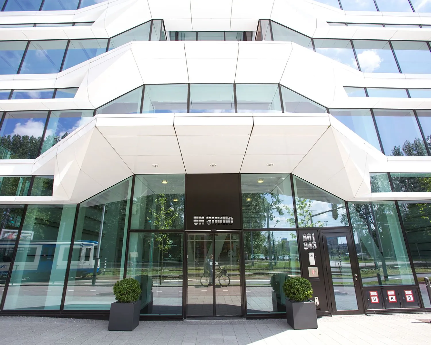 Voorgevel van het moderne kantoorgebouw van UNStudio met glazen wanden en witte architectonische elementen.