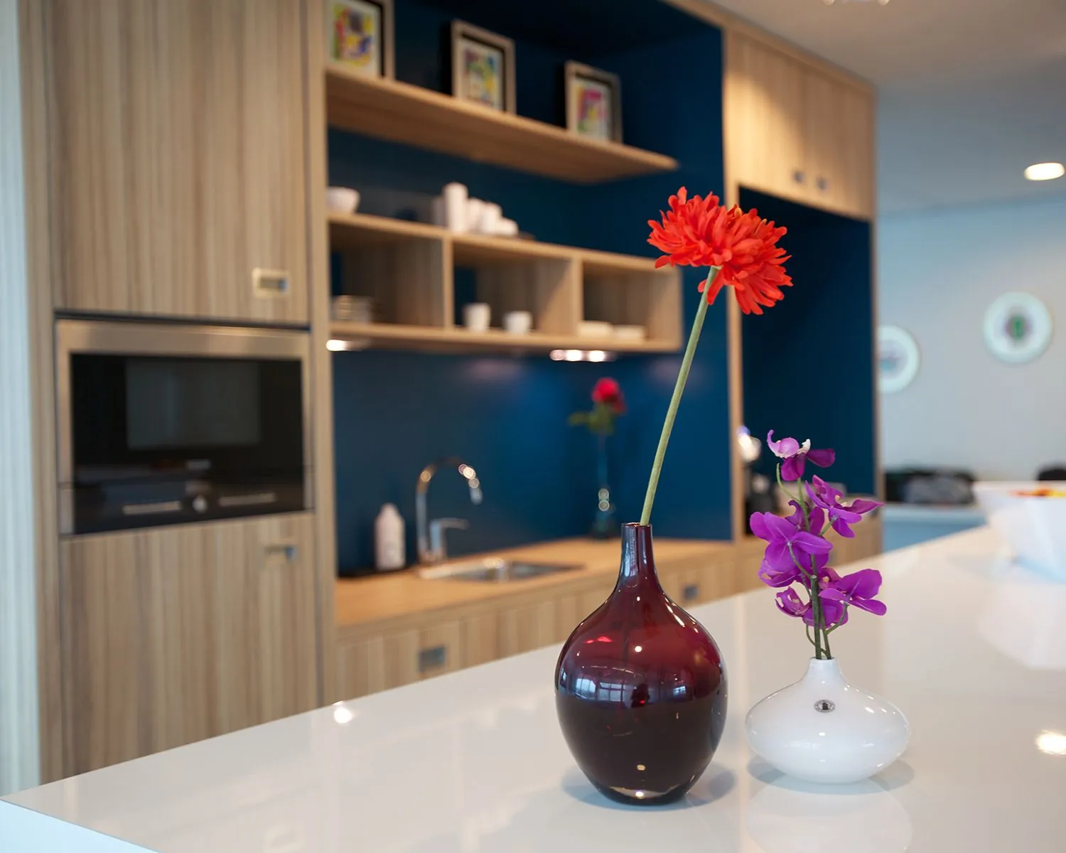 Moderne keuken met houten kasten, blauwe achterwand en twee vazen met bloemen op een wit kookeiland.