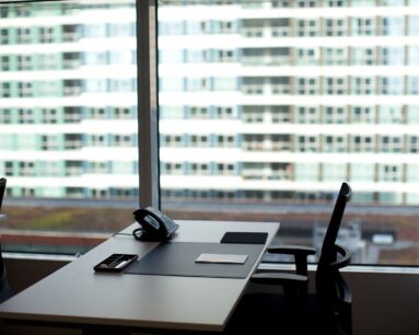 Modern kantoor met een leeg bureau, telefoontoestel en uitzicht op een hoog gebouw met glazen ramen.