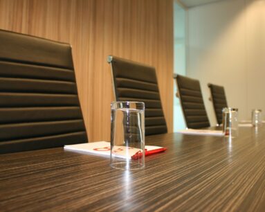 Vergaderruimte met zwarte lederen stoelen, glazen en notitieblokken op een houten tafel.