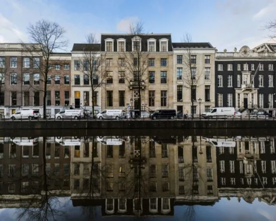Rij monumentale grachtenpanden met hun reflectie in het water aan een Amsterdamse gracht.