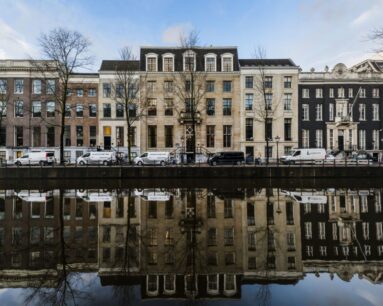 Rij statige grachtenpanden in Amsterdam weerspiegeld in het water van de gracht.