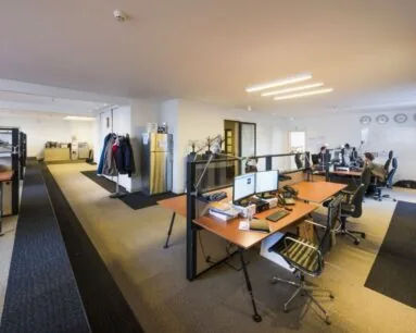 Moderne kantooruimte met meerdere bureaus, computers en enkele mensen aan het werk.