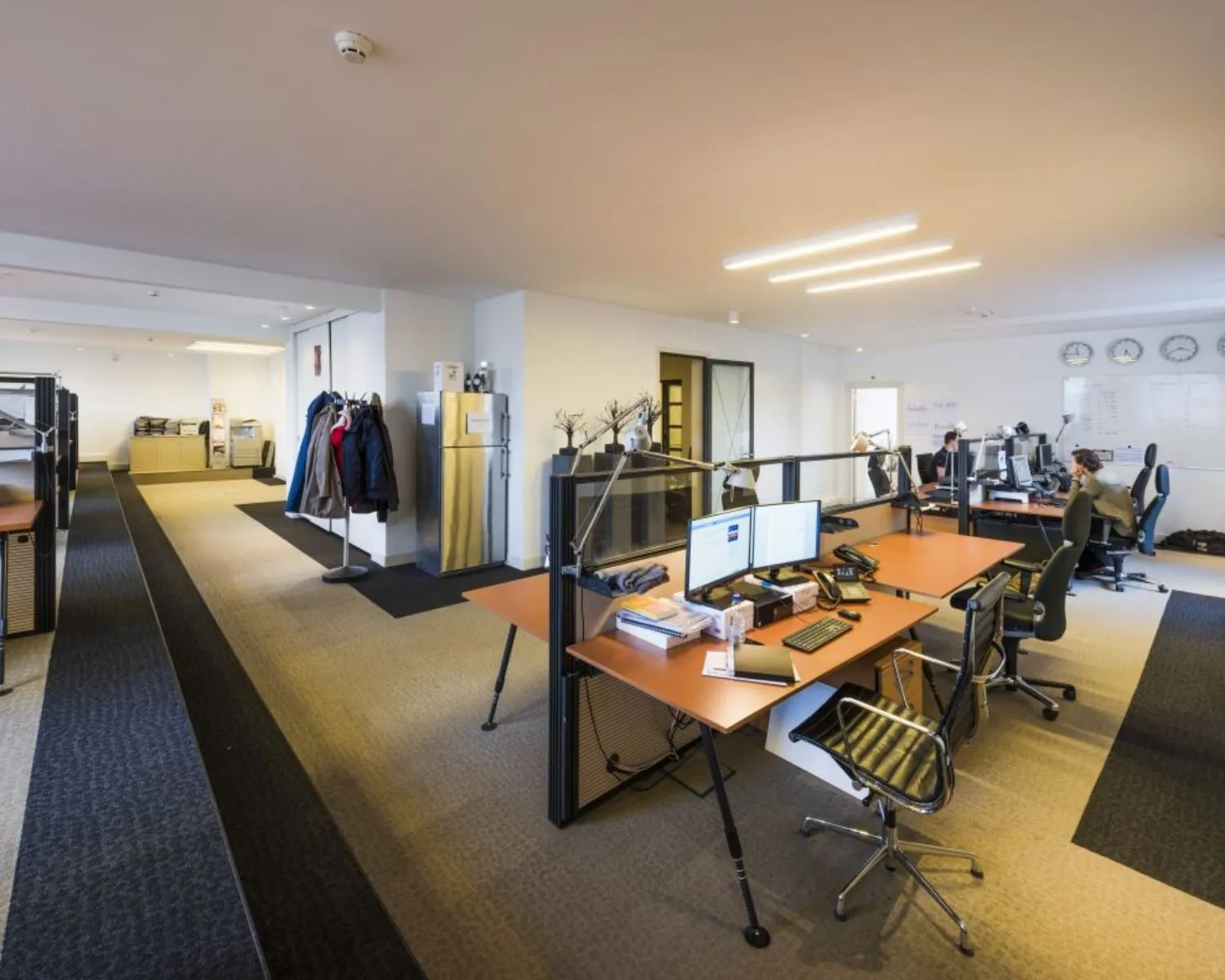 Moderne kantooruimte met meerdere bureaus, computers en enkele mensen aan het werk.