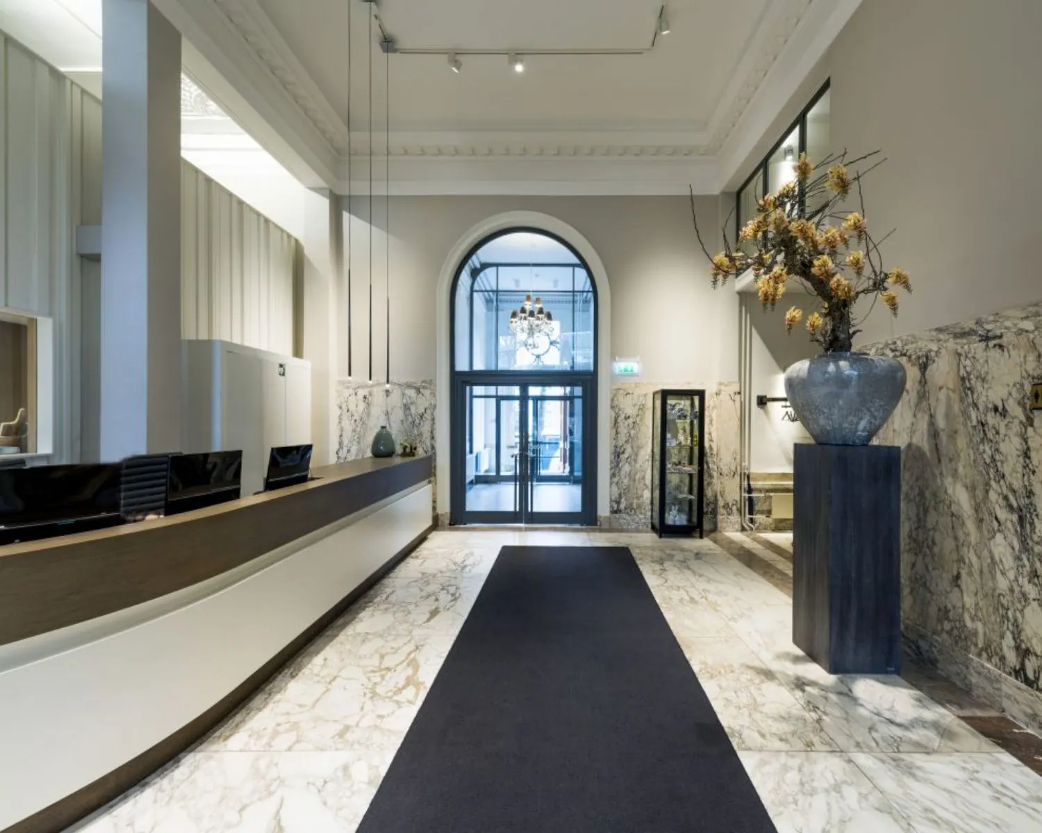 Luxe hotelreceptie met marmeren vloeren, hoge plafonds en een groot bloemstuk op een sokkel.