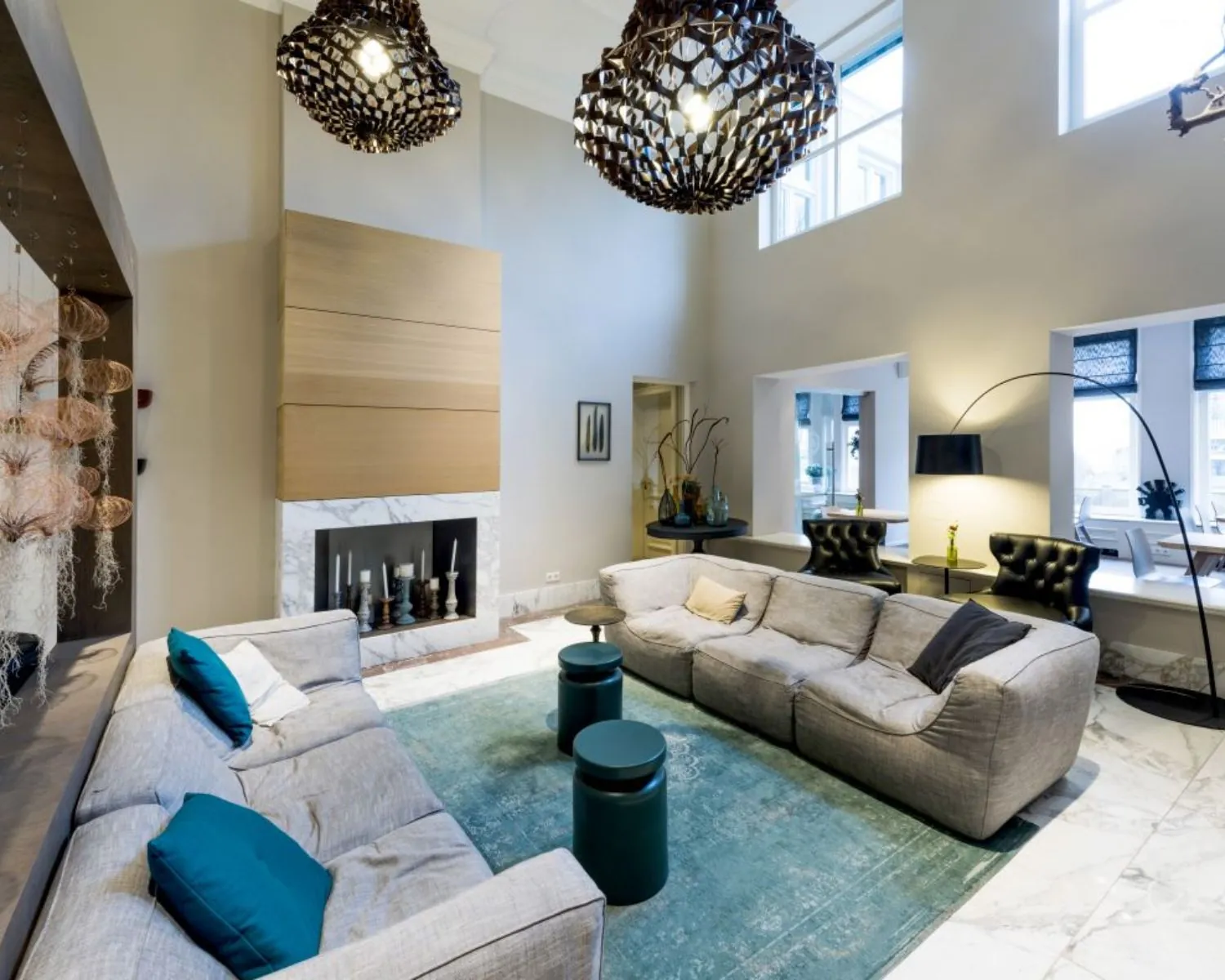 Moderne en ruime woonkamer met hoge plafonds, grijze banken, turquoise accenten en een marmeren open haard.
