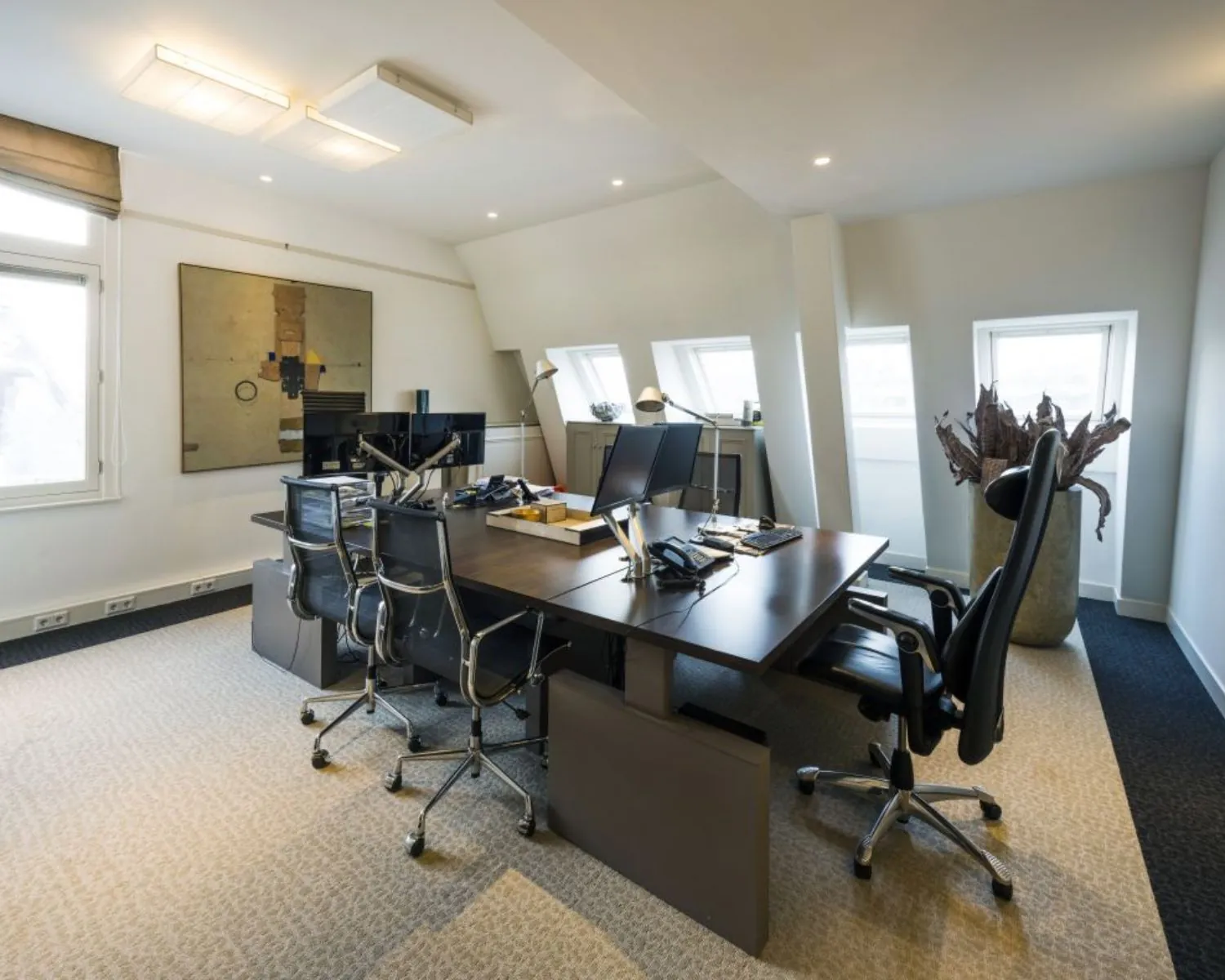 Modern ingericht kantoor met strakke bureaus, meerdere bureaustoelen, computeropstellingen en natuurlijke lichtinval via dakramen.