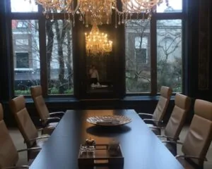 Luxe vergaderruimte met leren stoelen, kristallen kroonluchters en grote ramen met uitzicht op een tuin.