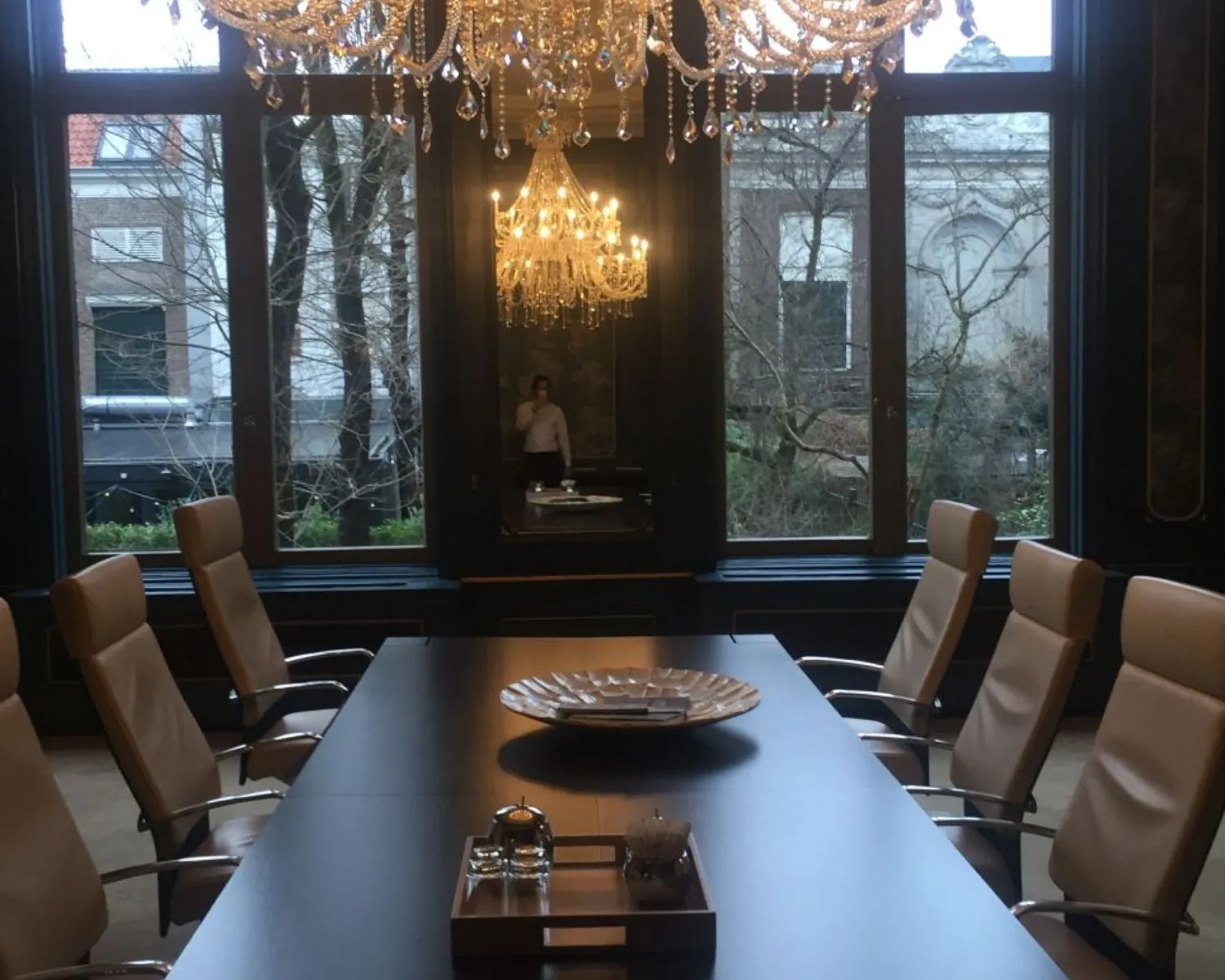 Luxe vergaderruimte met leren stoelen, kristallen kroonluchters en grote ramen met uitzicht op een tuin.