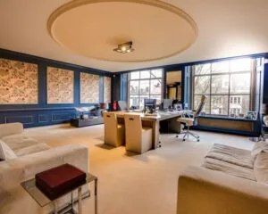 Luxueus ingericht kantoor met grote ramen, klassieke wandpanelen en moderne bureaus.