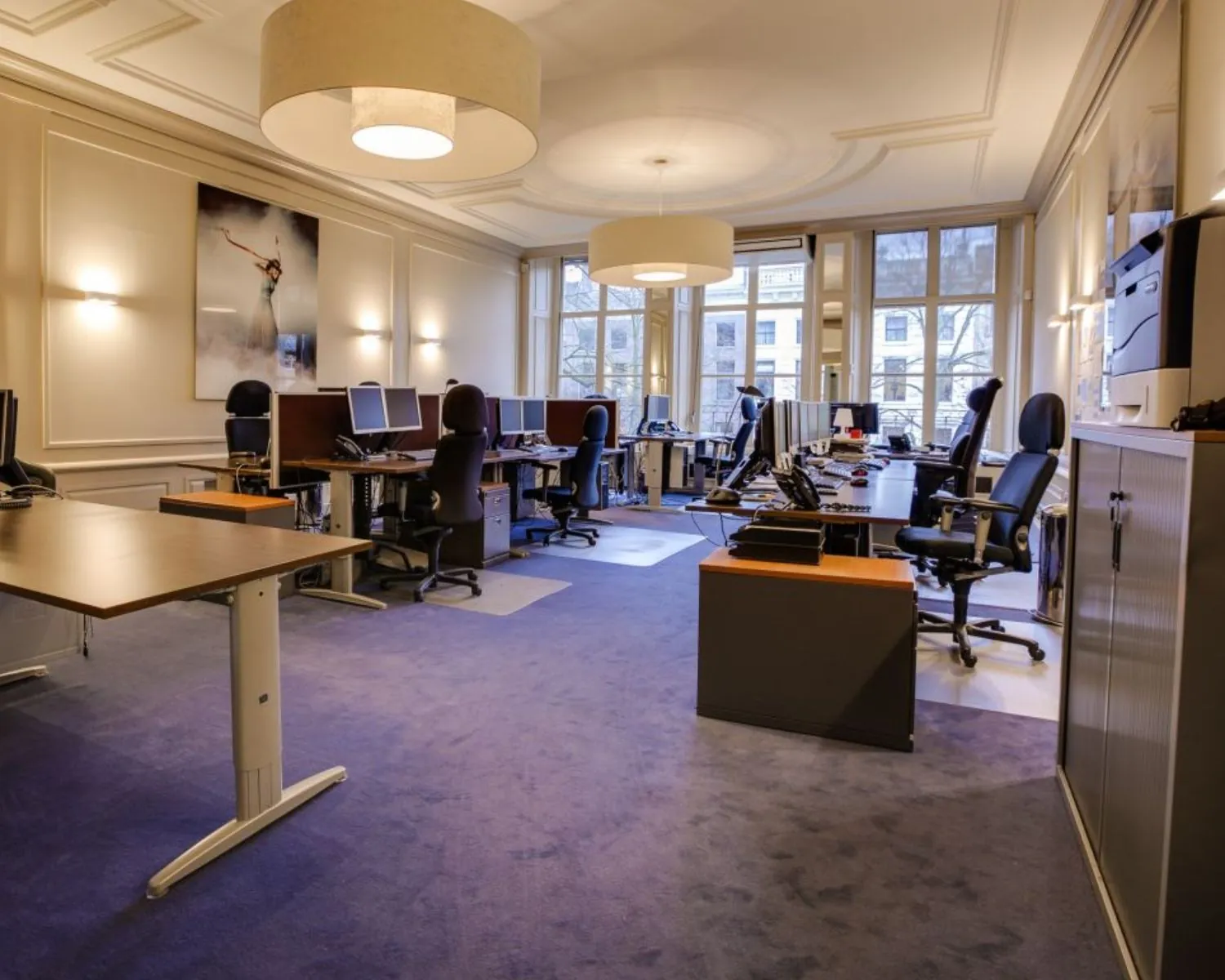 Ruim en modern kantoor met meerdere werkplekken, bureaustoelen en computers in een lichte omgeving met grote ramen.