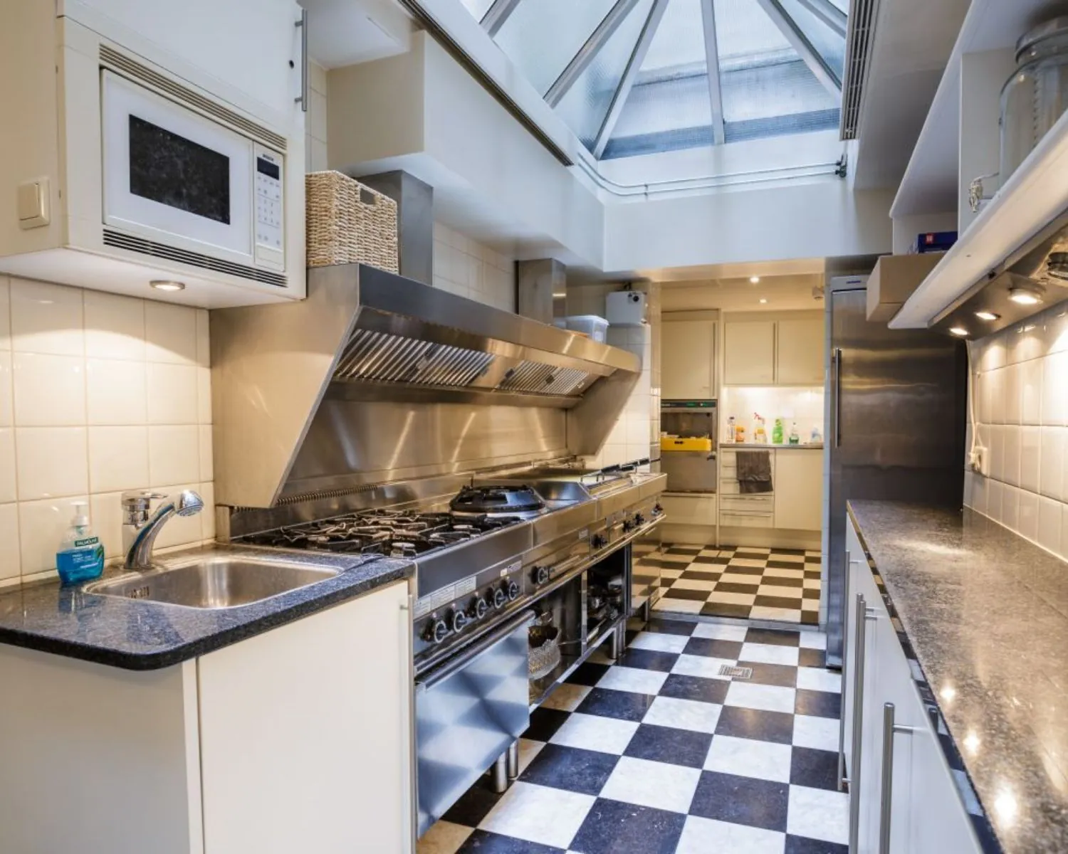 Professionele keuken met roestvrijstalen fornuis, zwart-wit geblokte vloer en glazen dak.