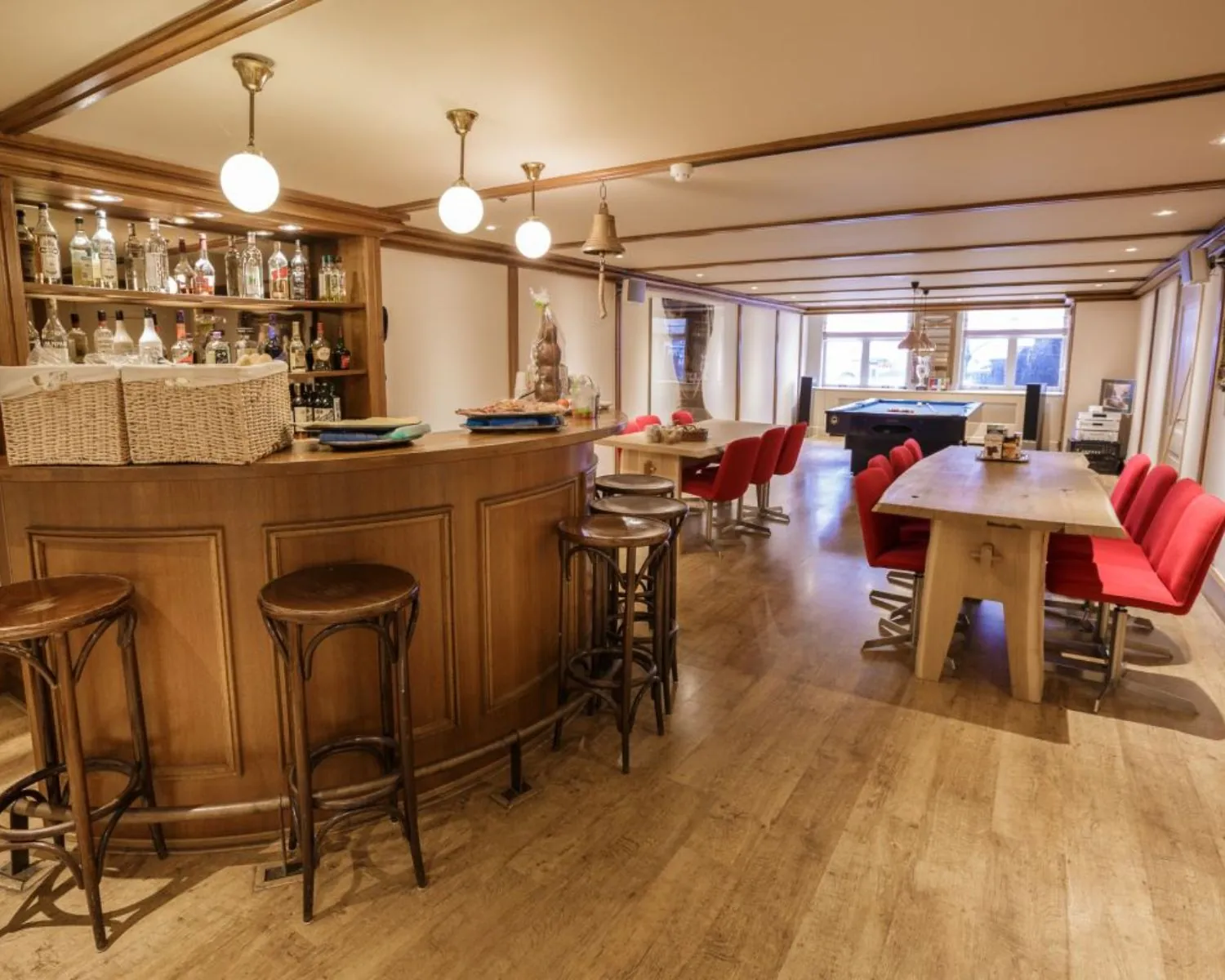 Sfeervol ingerichte recreatieruimte met houten bar, rode stoelen en een tafelvoetbaltafel.