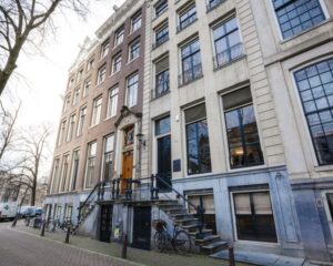 Gevel van een klassiek Amsterdams herenhuis met trapgevel en fietsen geparkeerd langs de gracht.