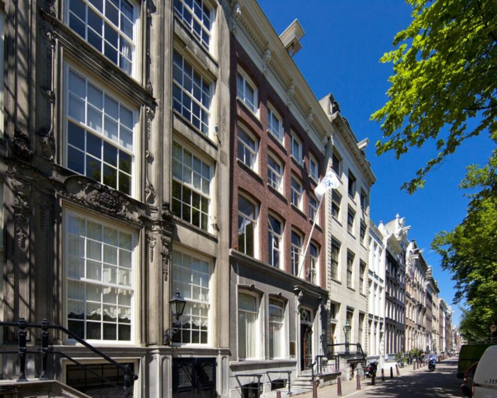 Rij met monumentale grachtenpanden aan een zonnige straat in Amsterdam.