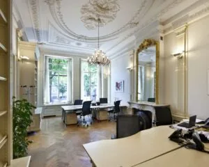 Elegante kantoorruimte met klassieke ornamenten, grote ramen en moderne werkplekken.