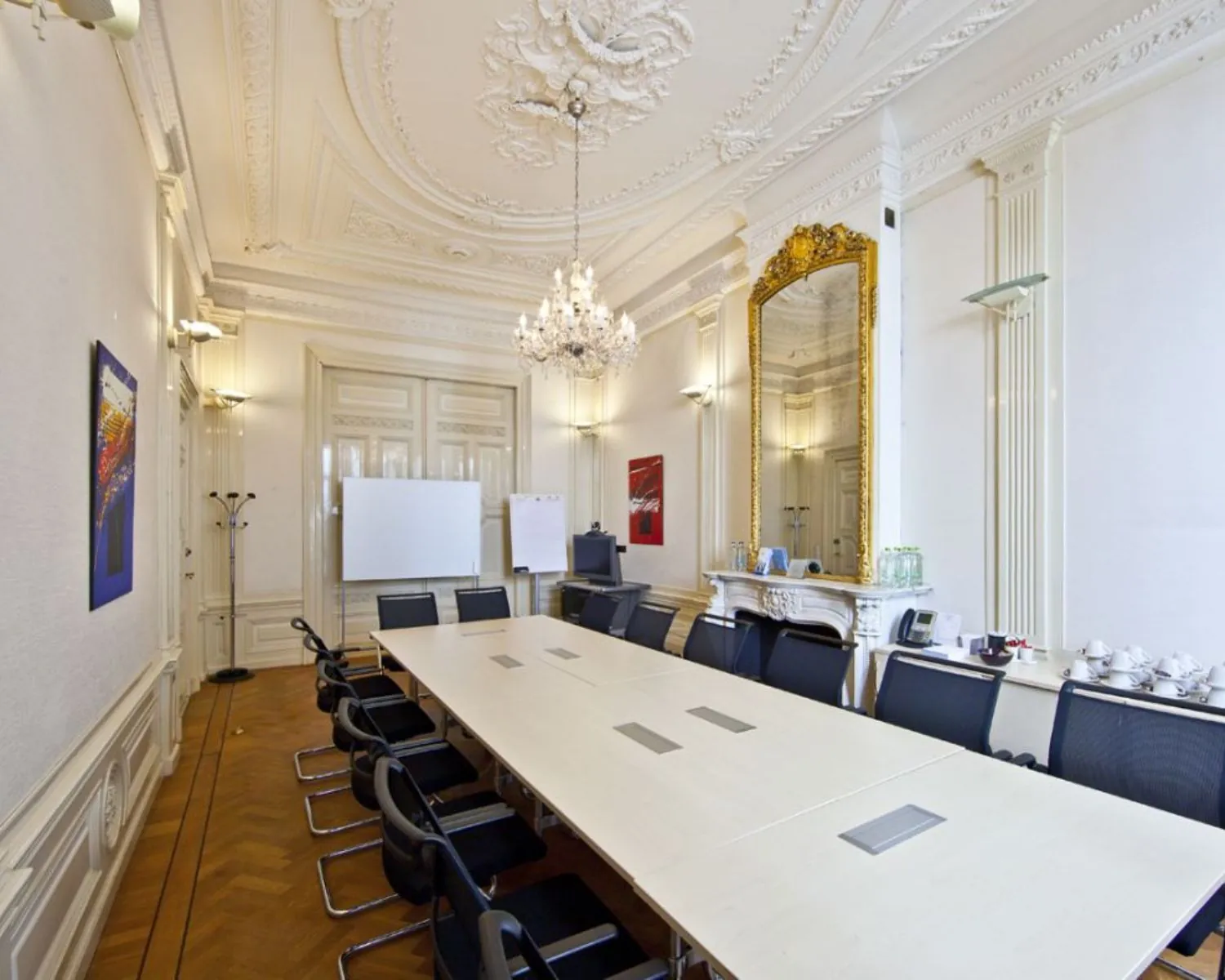 Vergaderruimte in klassieke stijl met een lange tafel, moderne stoelen, kroonluchter en groot verguld spiegel boven een sierlijke open haard.
