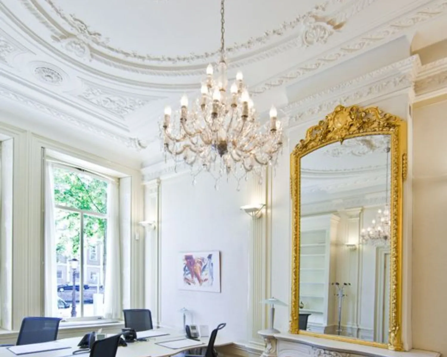 Luxe kantoorruimte met klassieke ornamenten, kroonluchter en grote vergulde spiegel.