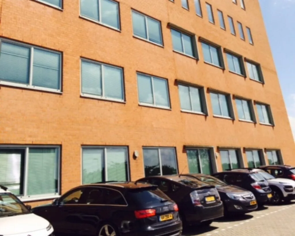 Gebouw met oranje bakstenen gevel en geparkeerde auto's ervoor op een zonnige dag.