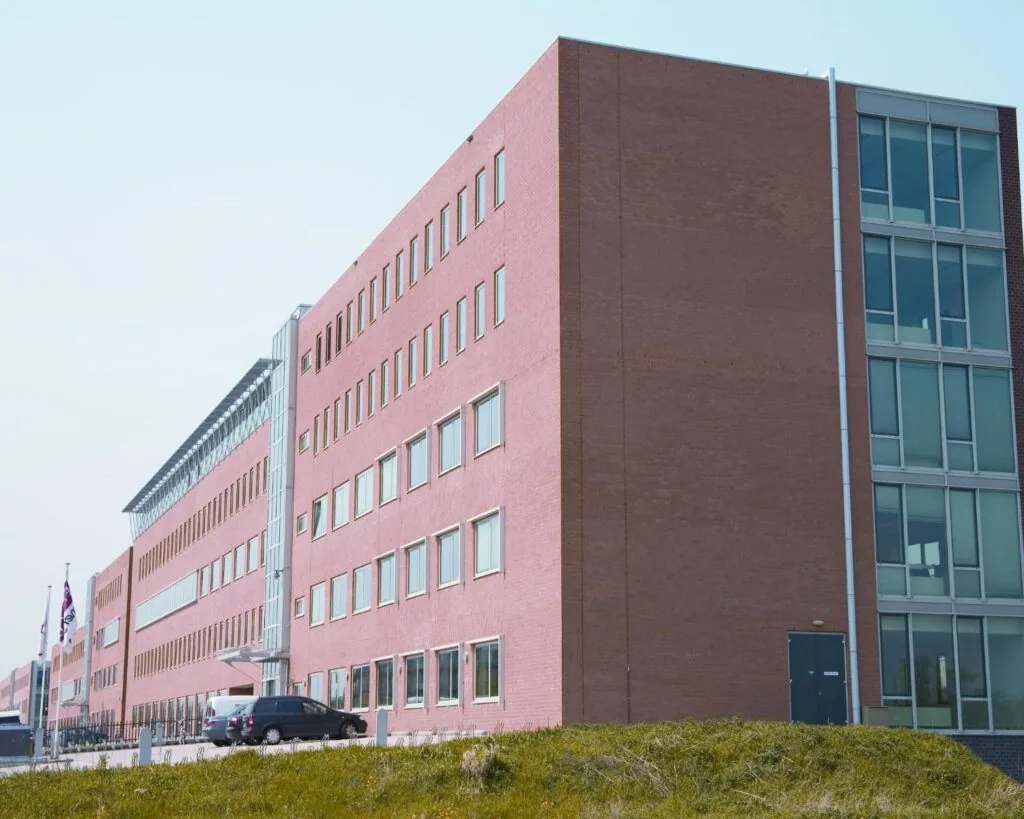 Modern rood bakstenen kantoor- of overheidsgebouw met meerdere verdiepingen en grote ramen.