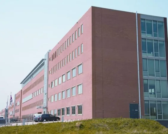 Modern rood bakstenen kantoor- of overheidsgebouw met meerdere verdiepingen en grote ramen.