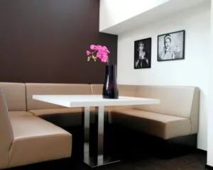 Moderne zithoek met beige banken, een witte tafel, een donkere vaas met roze bloemen en twee zwart-wit portretten aan de muur.