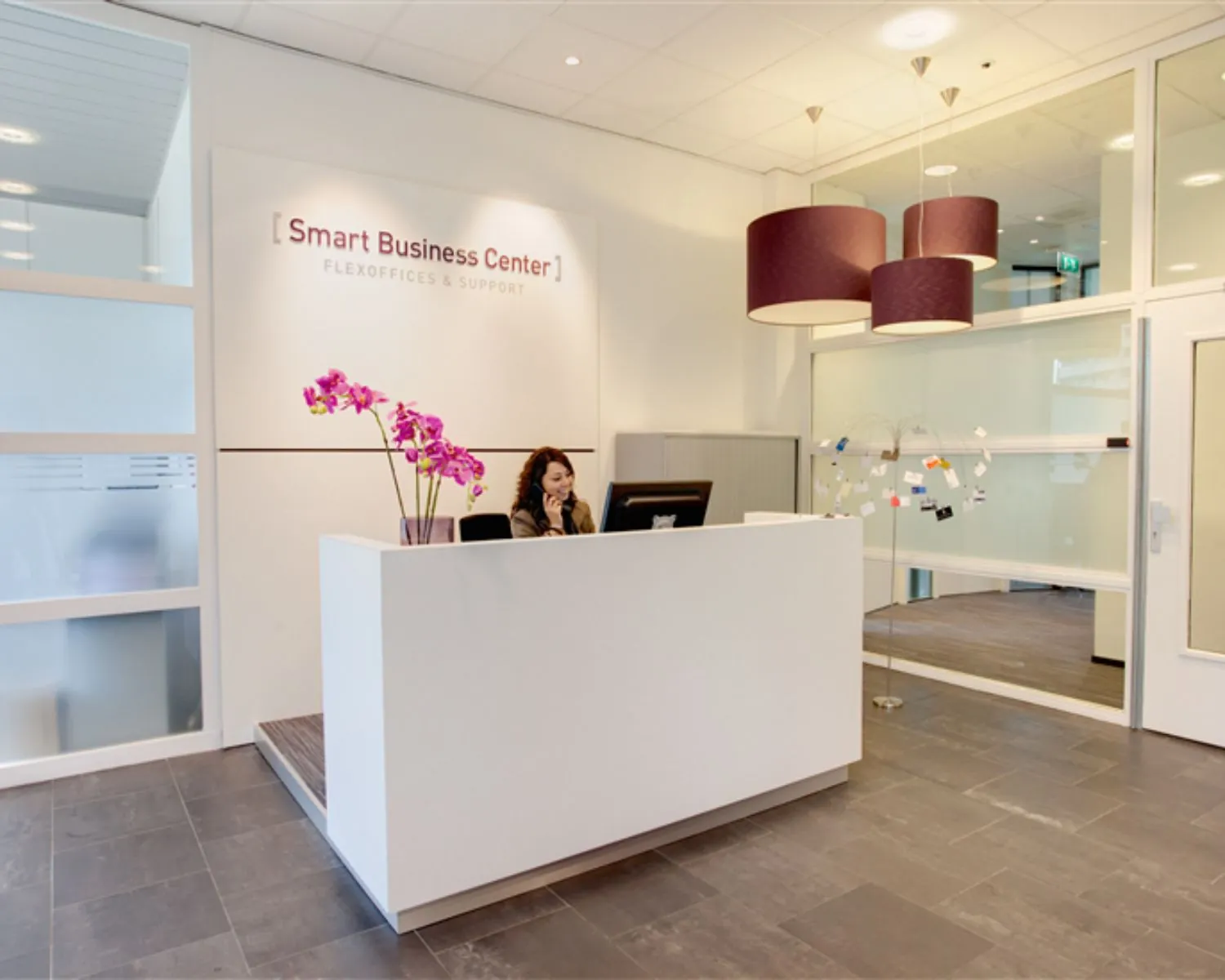 Receptiebalie van Smart Business Center met een receptioniste achter een computer en paarse hanglampen erboven.